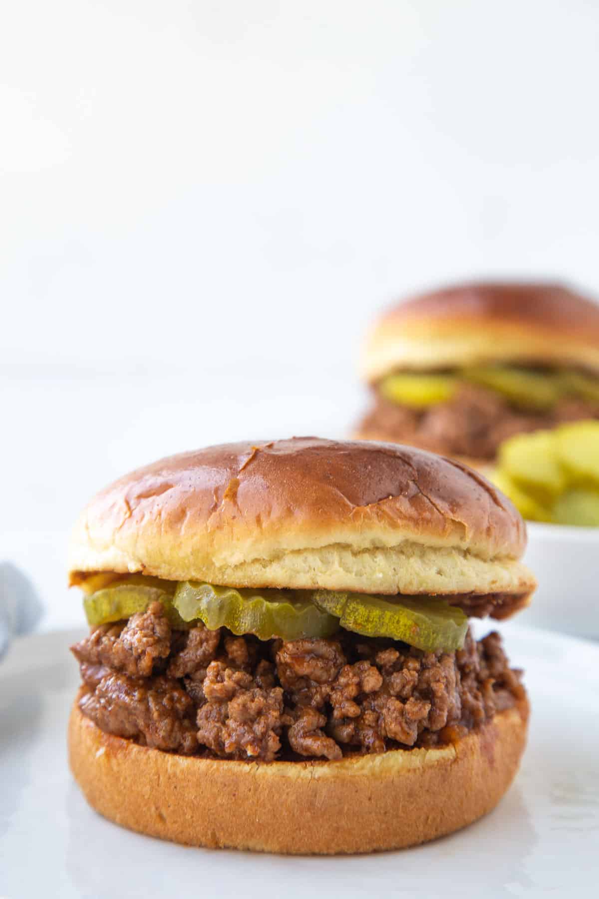 old fashioned sloppy joe sandwich on brioche with pickle chips, sitting on a white plate.