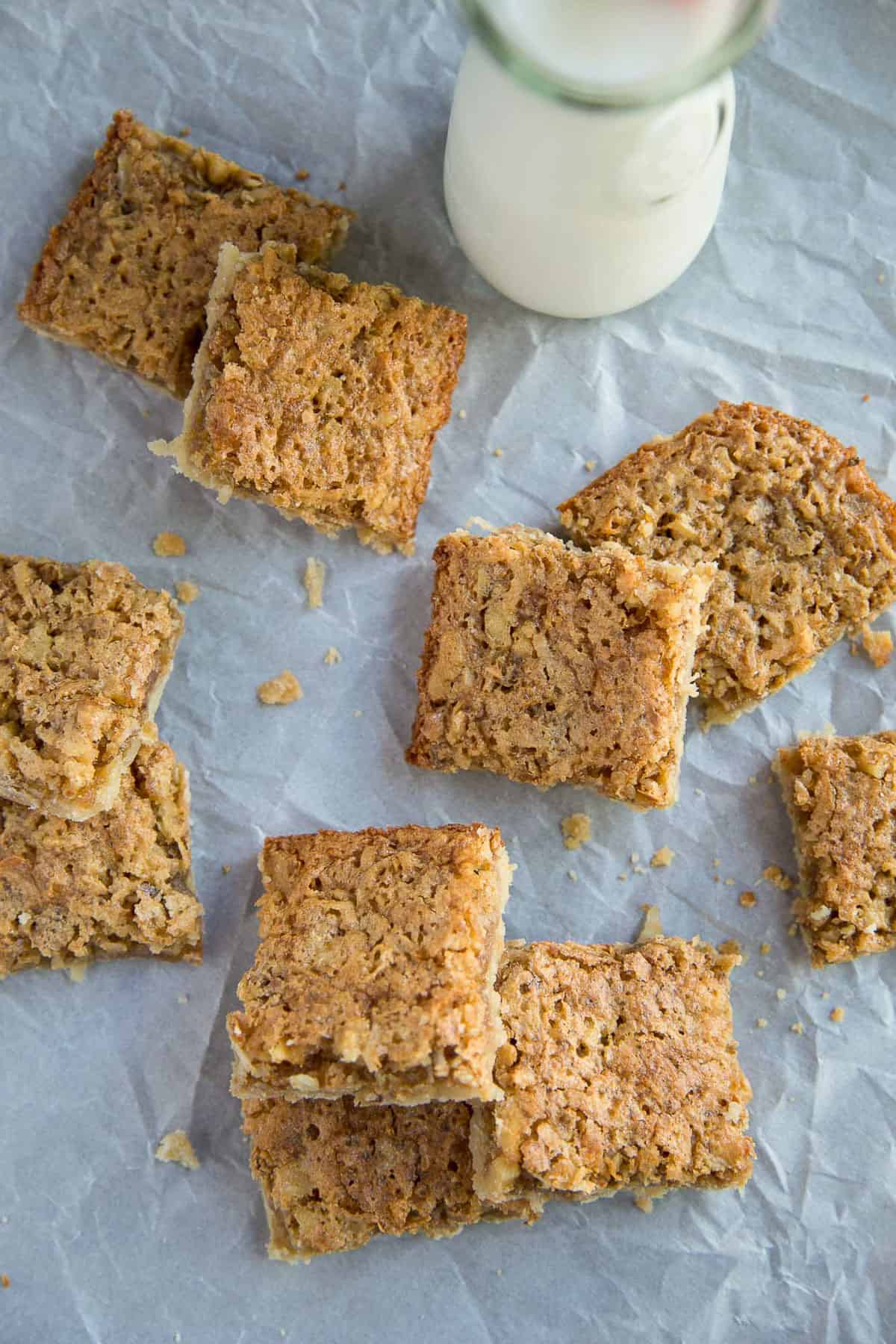 square coconut bars on white parchment next to a glass of milk.