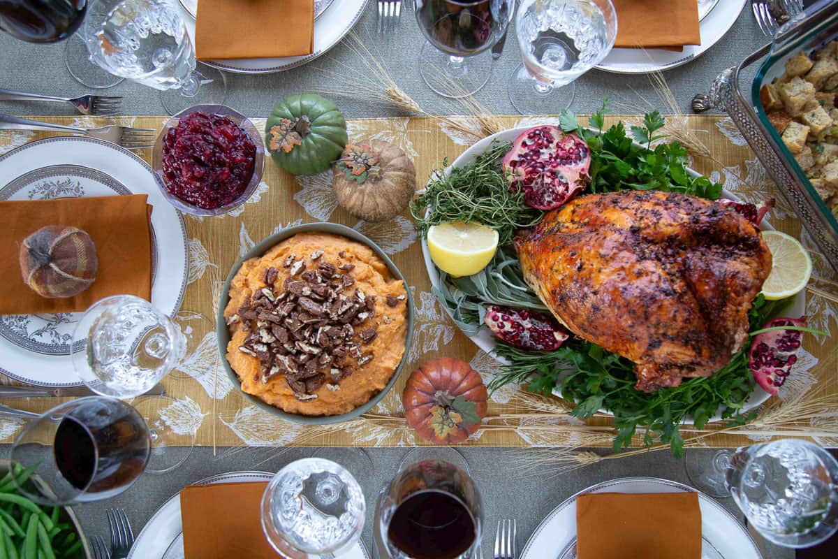 table set for thanksgiving dinner with a turkey breast, sweet potatoes topped iwth pecans, cranberry sauce, china plates, and orange napkins.