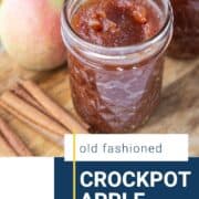 apple butter in a mason jar next to whole apples and cinnamon sticks.