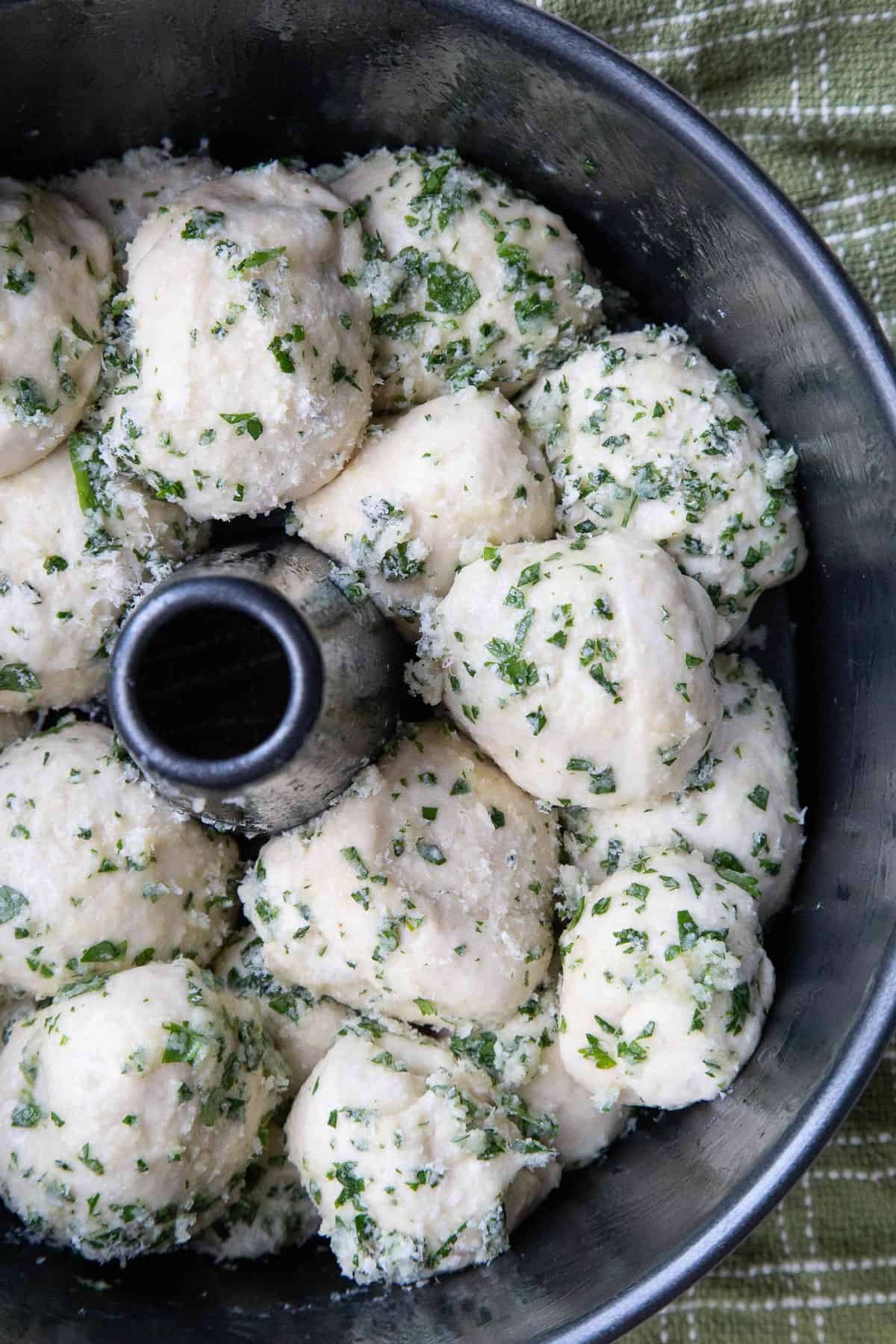 bread dough balls covered with parmesan and parsley in a tube pan.