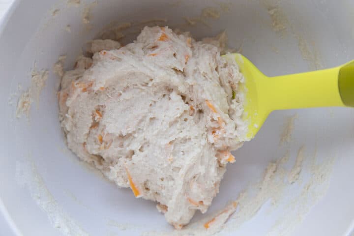 biscuit dough with shredded cheddar in it, in a white bowl with a yellow spatula.