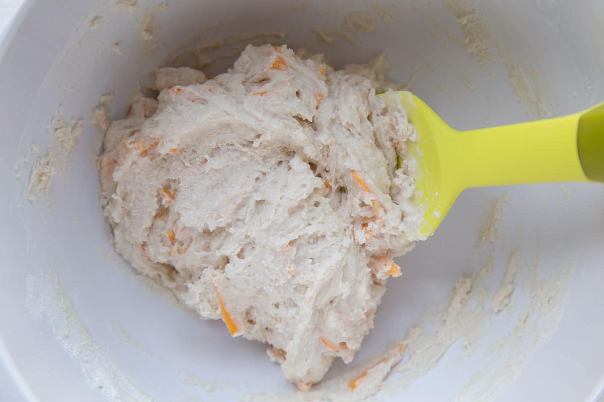 biscuit dough with shredded cheddar in it, in a white bowl with a yellow spatula.