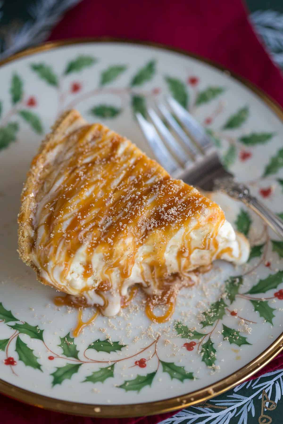 slice of eggnog pie drizzled with caramel and a fork on a decorative red and green plate.