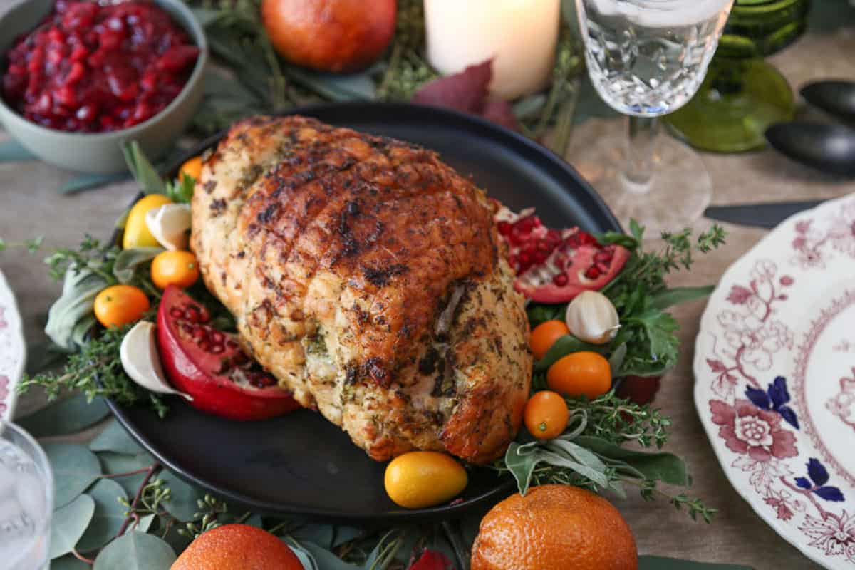 boneless turkey breast on a black platter surrounded by herbs and fresh fruits.