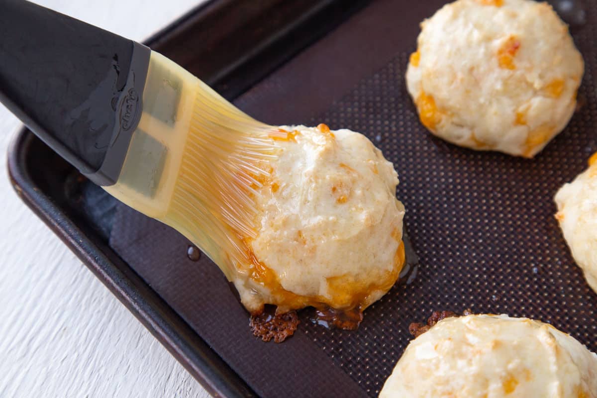 pastry brush brushing biscuits with melted butter on a sheet pan.