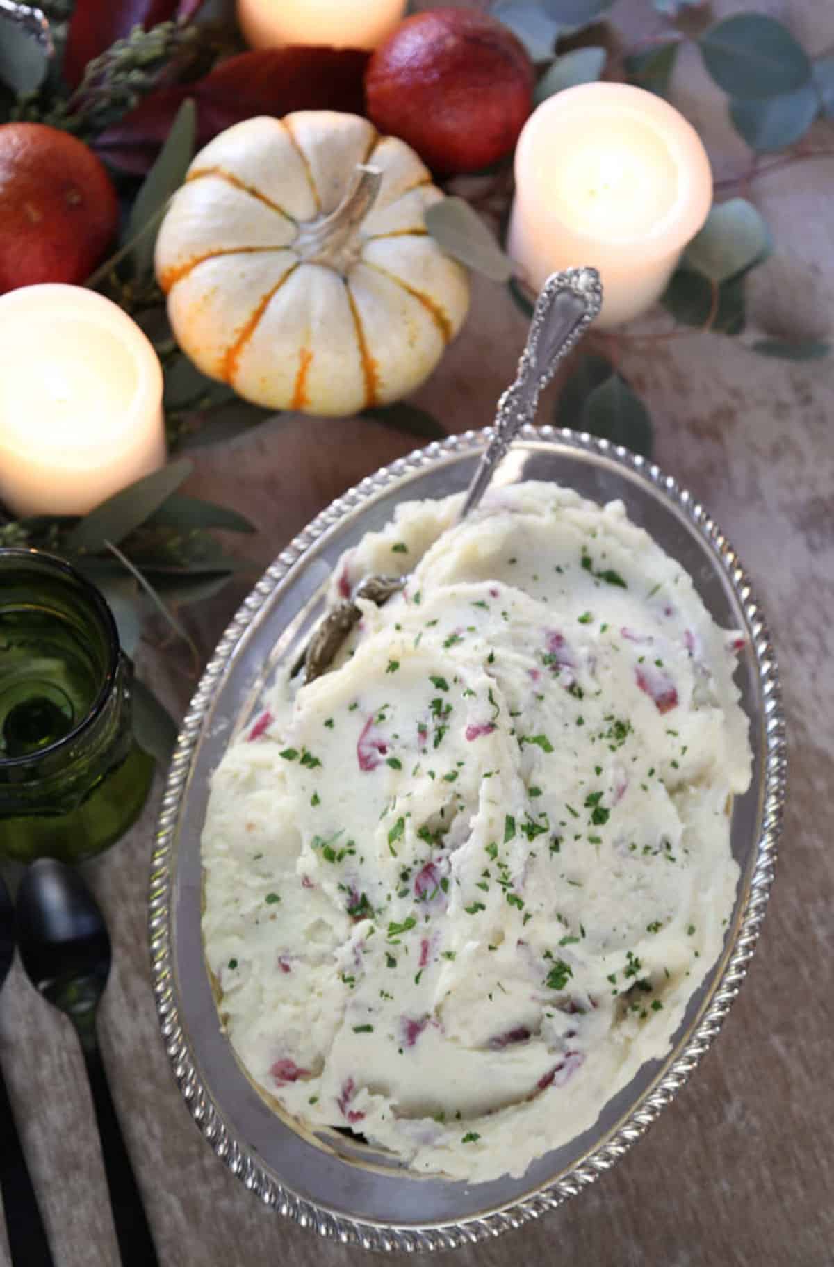 buttermilk mashed potatoes in a metal oval dish surrounded by candles and mini pumpkins.