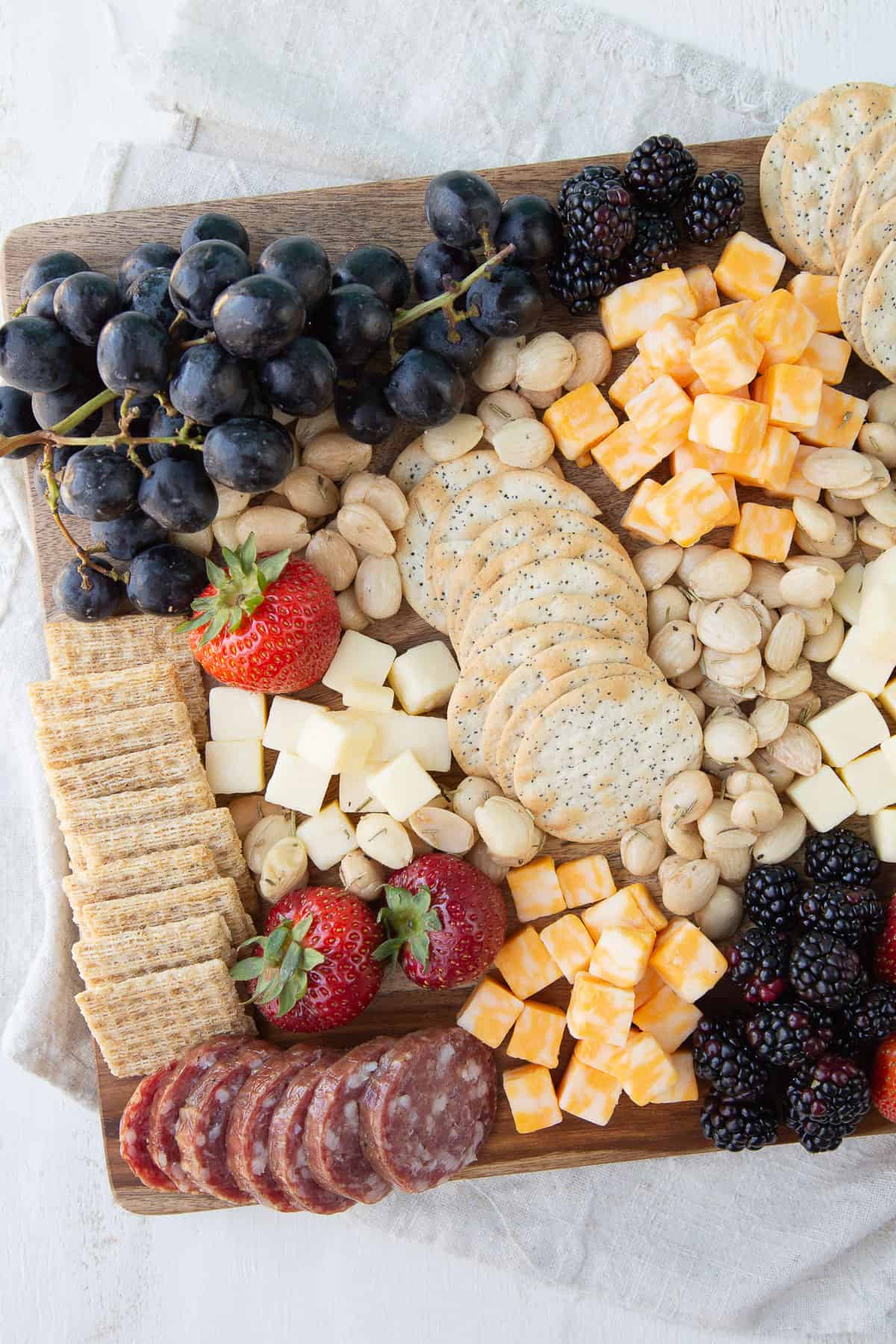 grapes, strawberries, crackers, cheese cubes, and almonds on a wooden board.