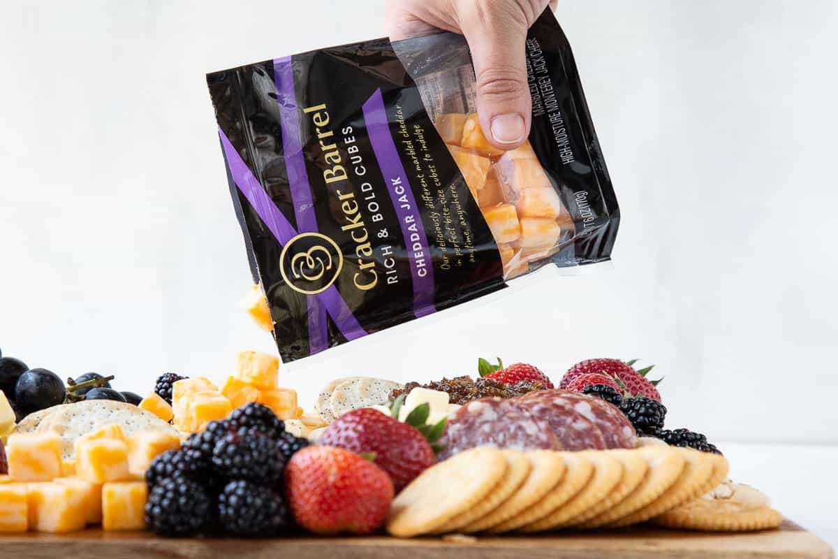 hand pouring cheese cubes from a package onto a cheese board.