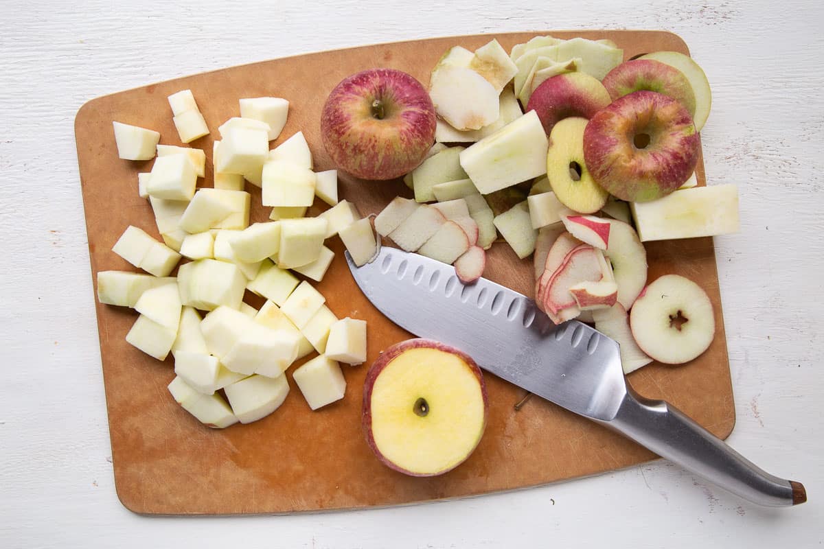 diced apples, whole apples, and apple peels on a cutting board with a knife.