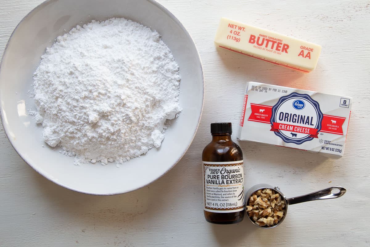 cream cheese, powdered sugar, butter, vanilla, and chopped walnuts on a white table.