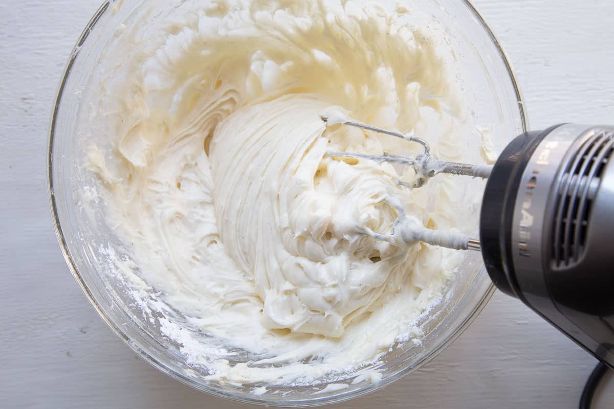 cream cheese frosting in a glass bowl with a hand mixer.