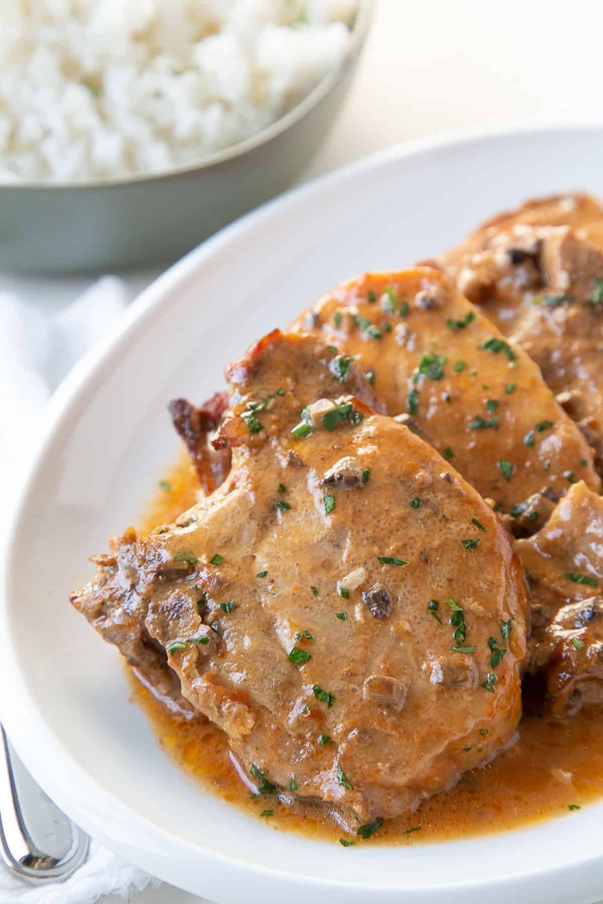 pork chops on a white platter topped with a brown sauce and chopped parsley. 