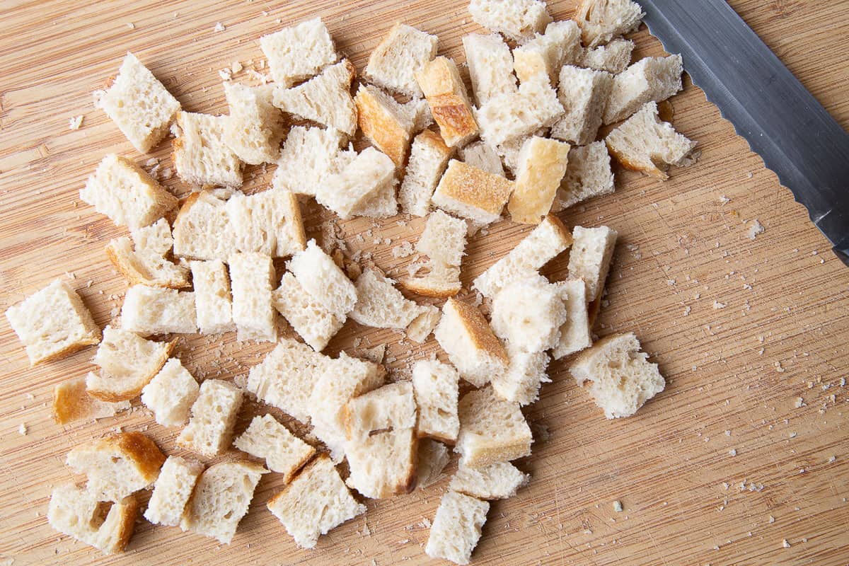cubed pieces of bread on a wooden cutting board.