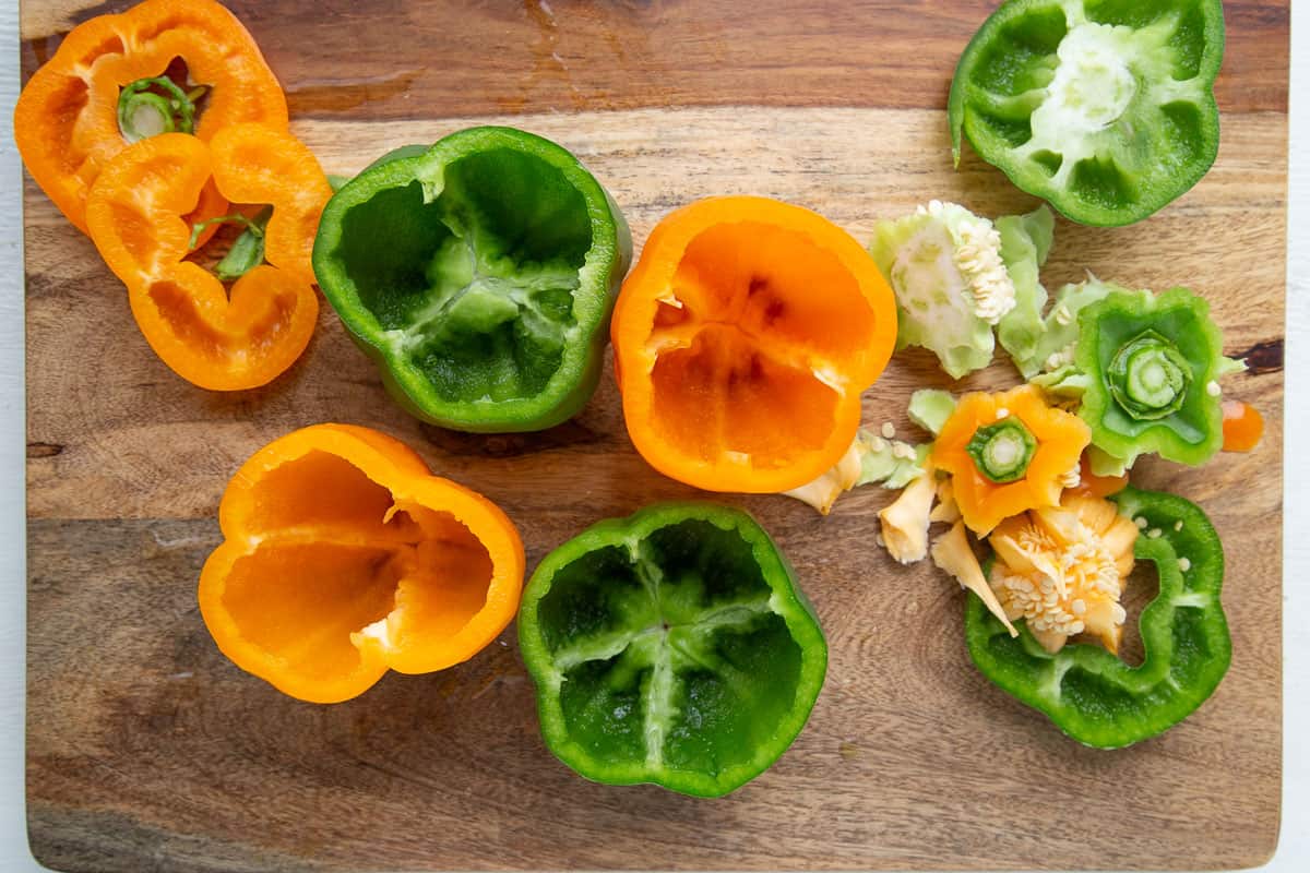 bell peppers with the tops sliced off on a wooden cutting board.