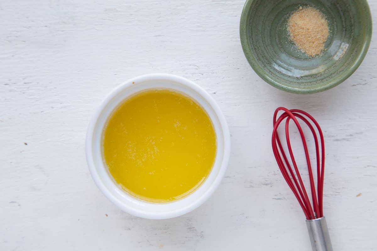 ramekins of butter and garlic powder next to a small red whisk.