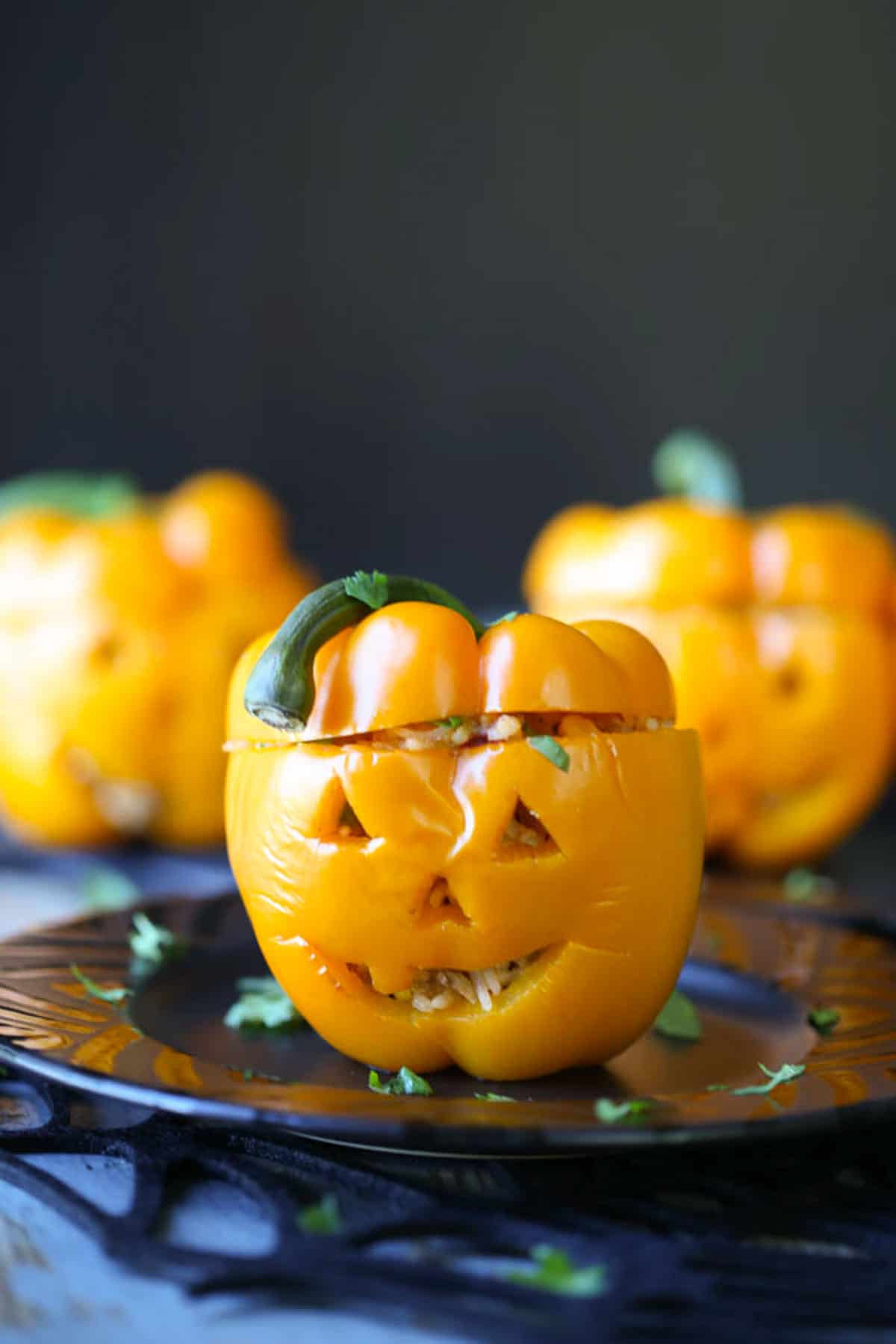 orange bell peppers with jack o lantern faces carved into them, sitting on a black plate.