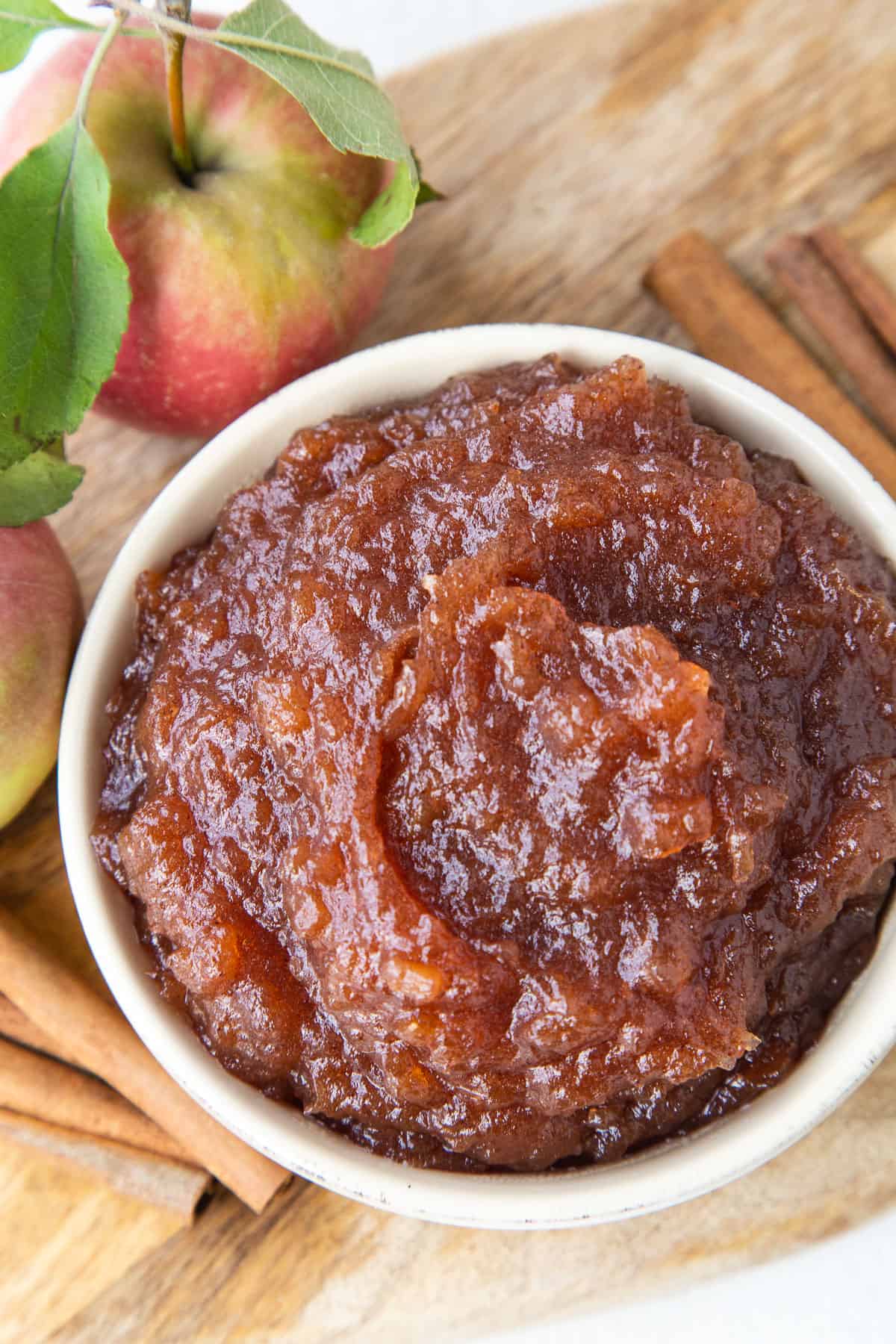 apple butter in a small yellow dish surrounded by cinnamon sticks and whole apples.