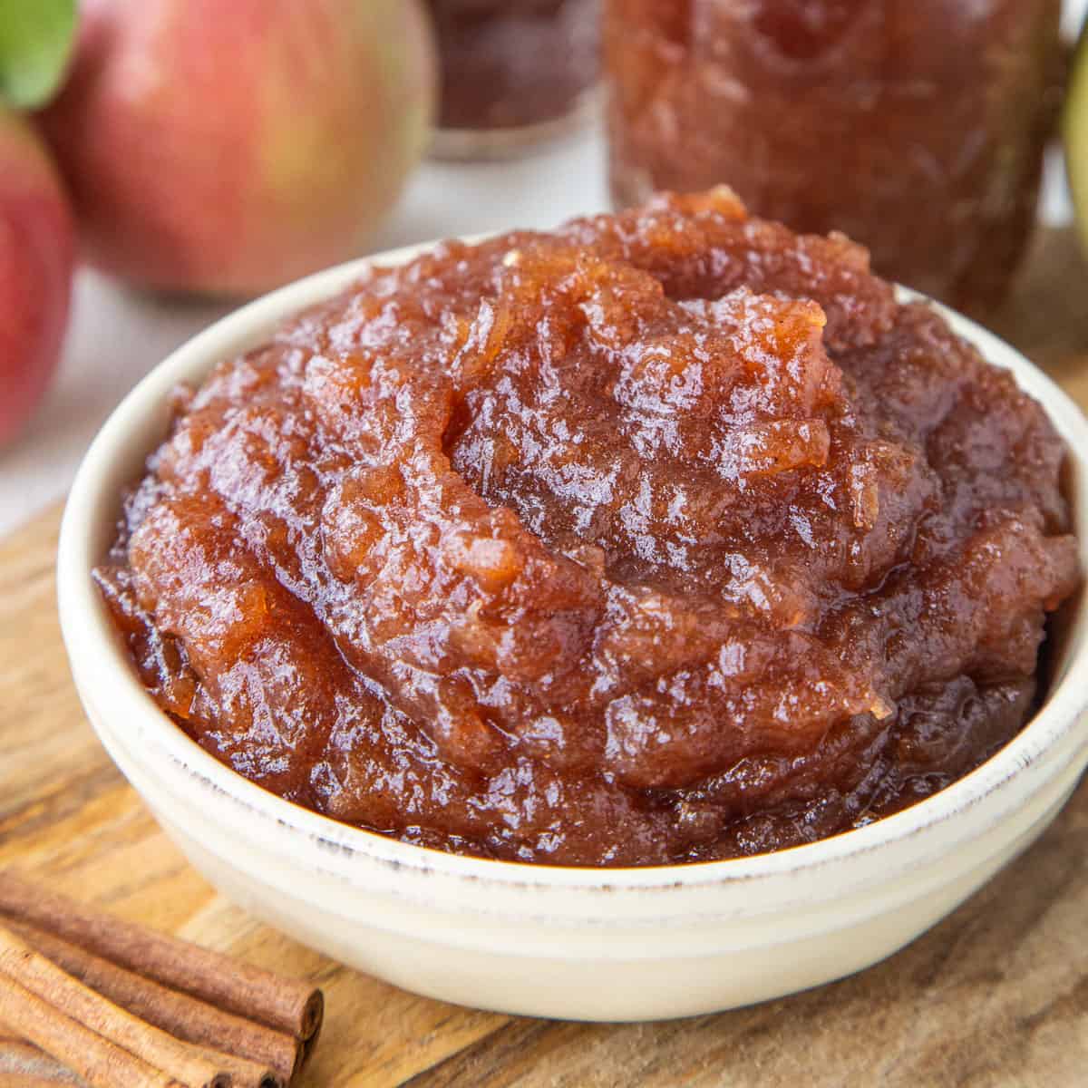 crockpot apple butter in a yellow dish next to whole apples and cinnamon sticks.