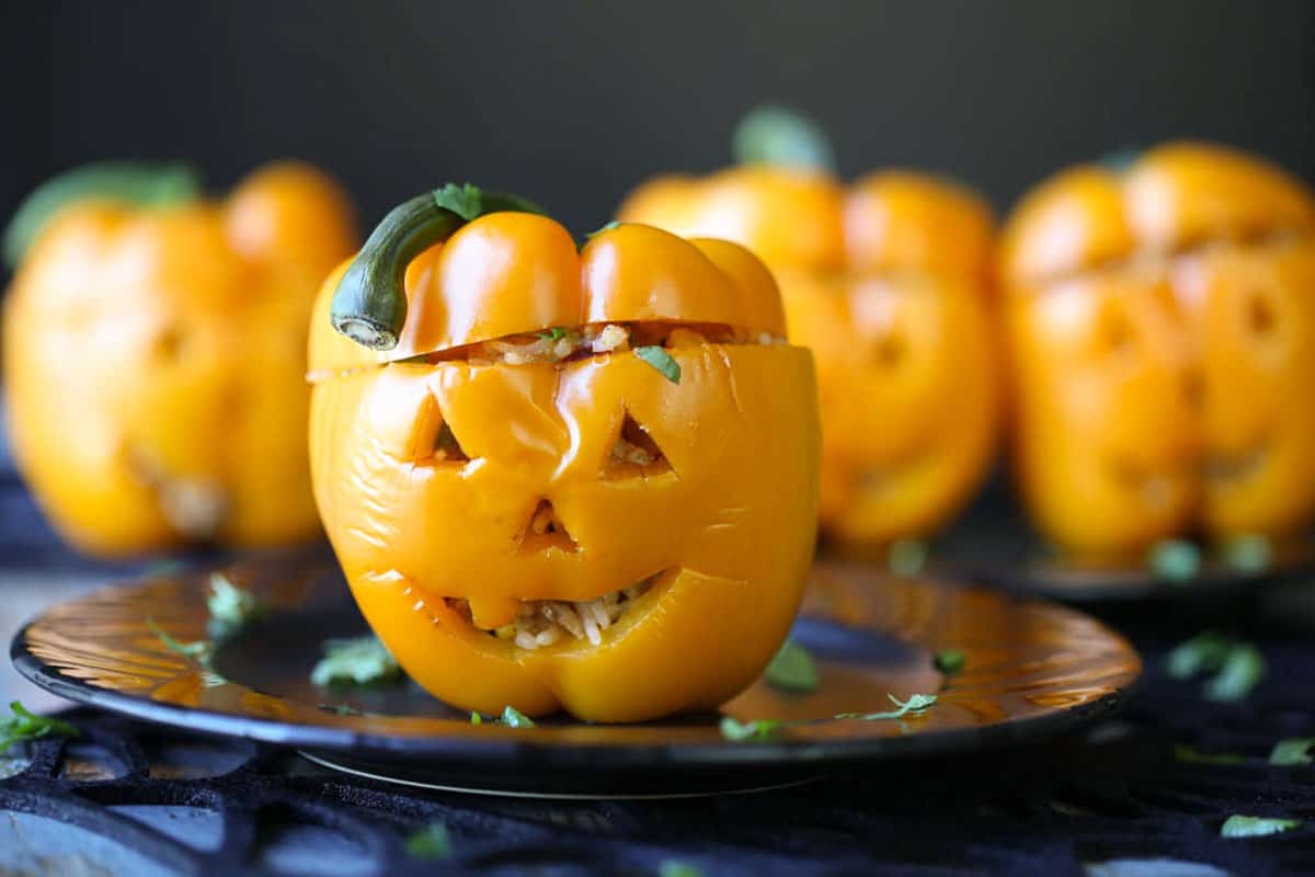 orange bell peppers with jack o lantern faces on a black plate.