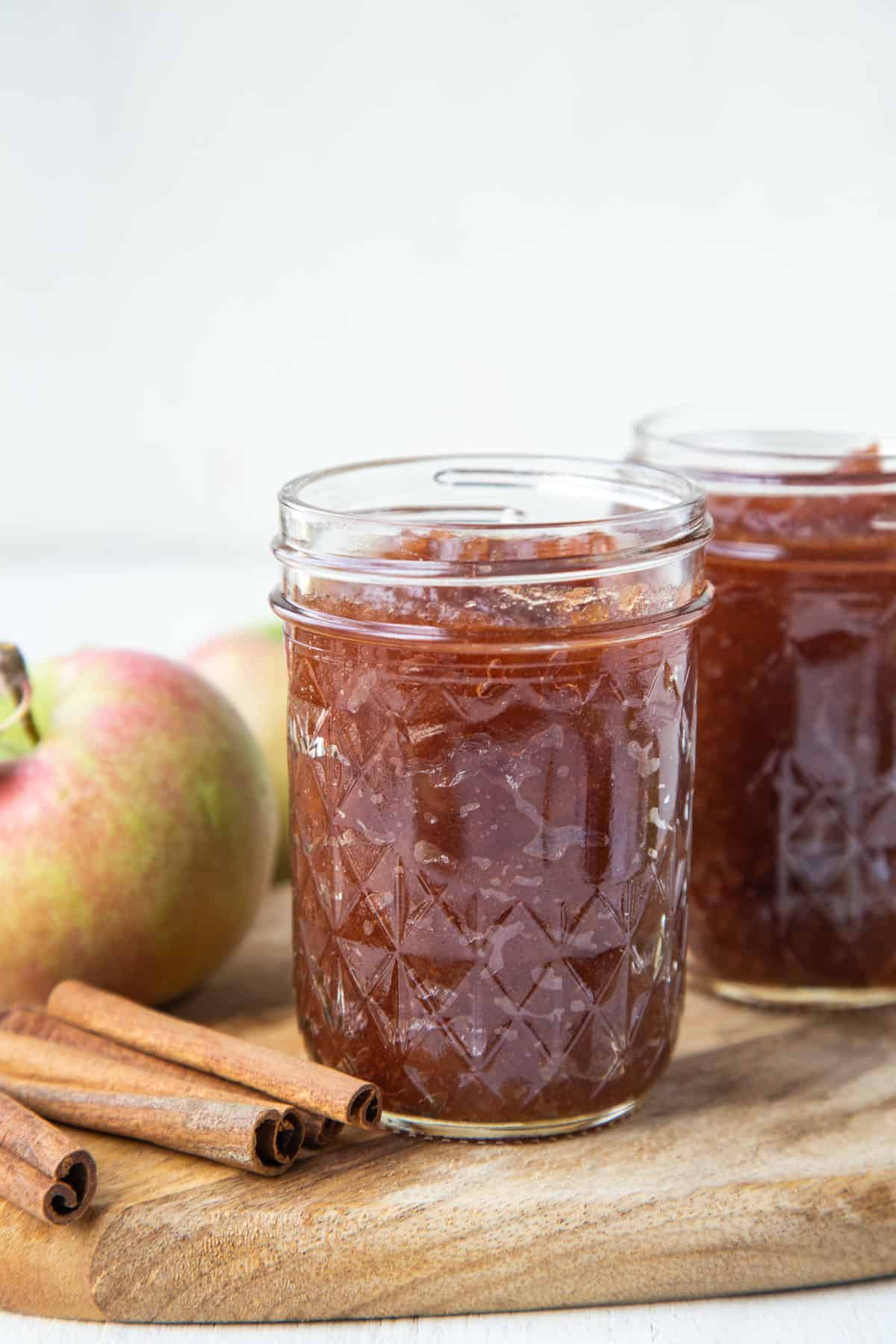 mason jars filled with apple butter next to cinnamon sticks and a whole apple.