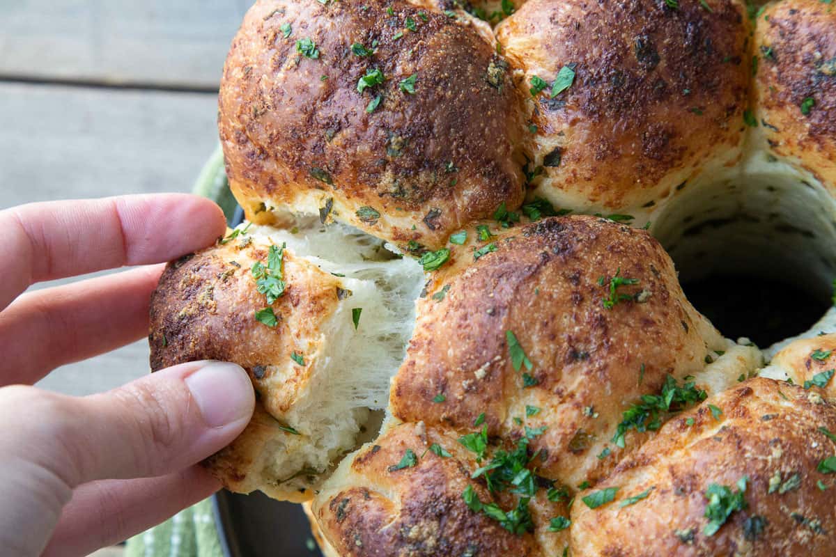 hand pulling a piece of garlic bread off a loaf.