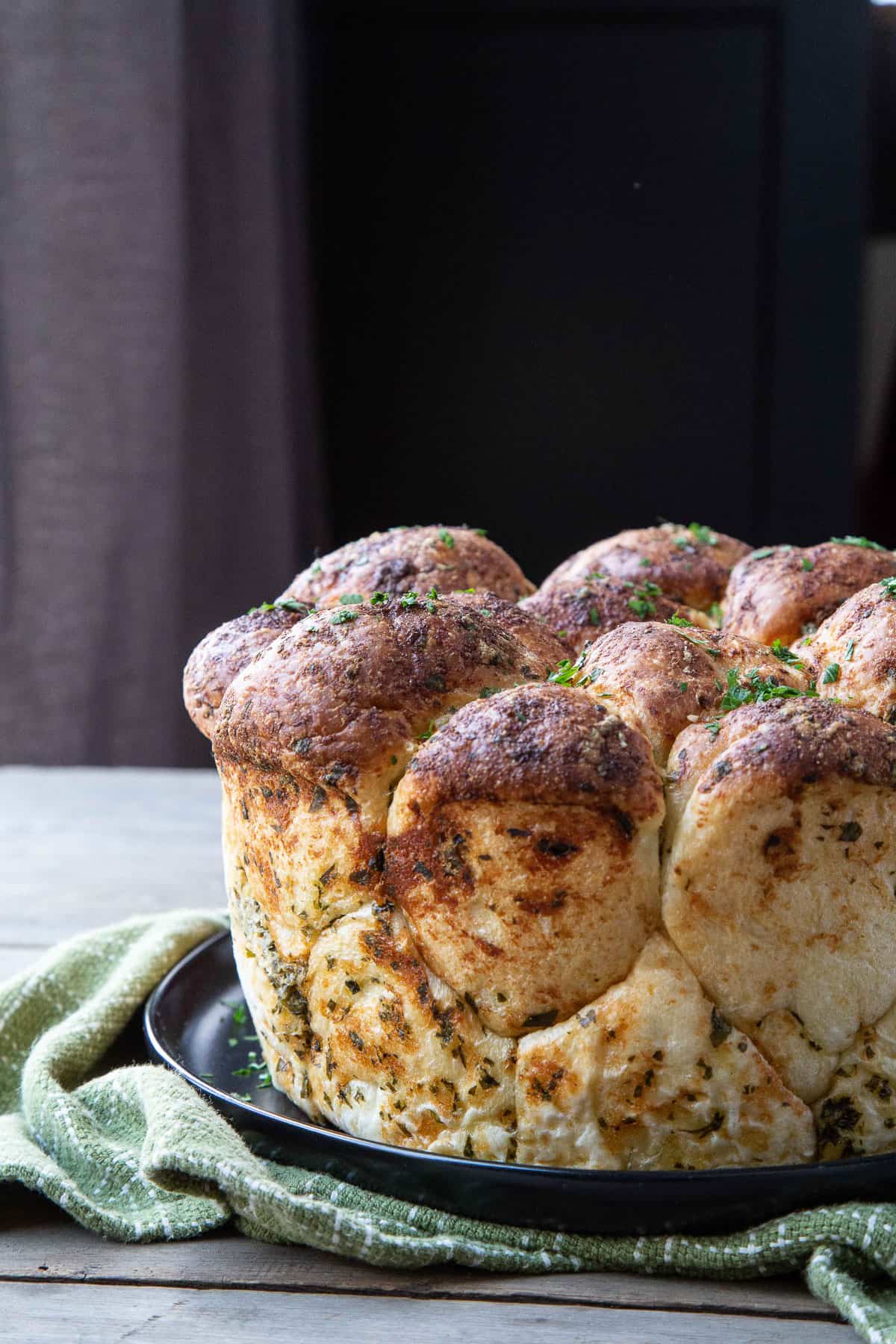 pull apart garlic bread on a black plate on top of a green tea towel.