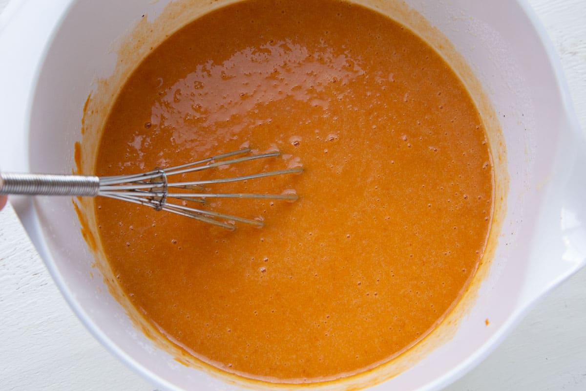 pumpkin cake batter in white bowl with a whisk.