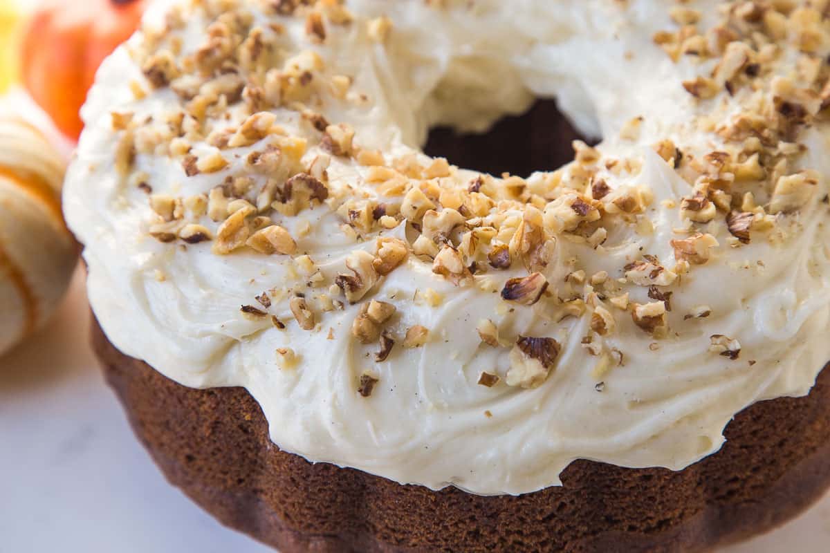 a whole pumpkin bundt cake topped with cream cheese frosting and chopped walnuts.