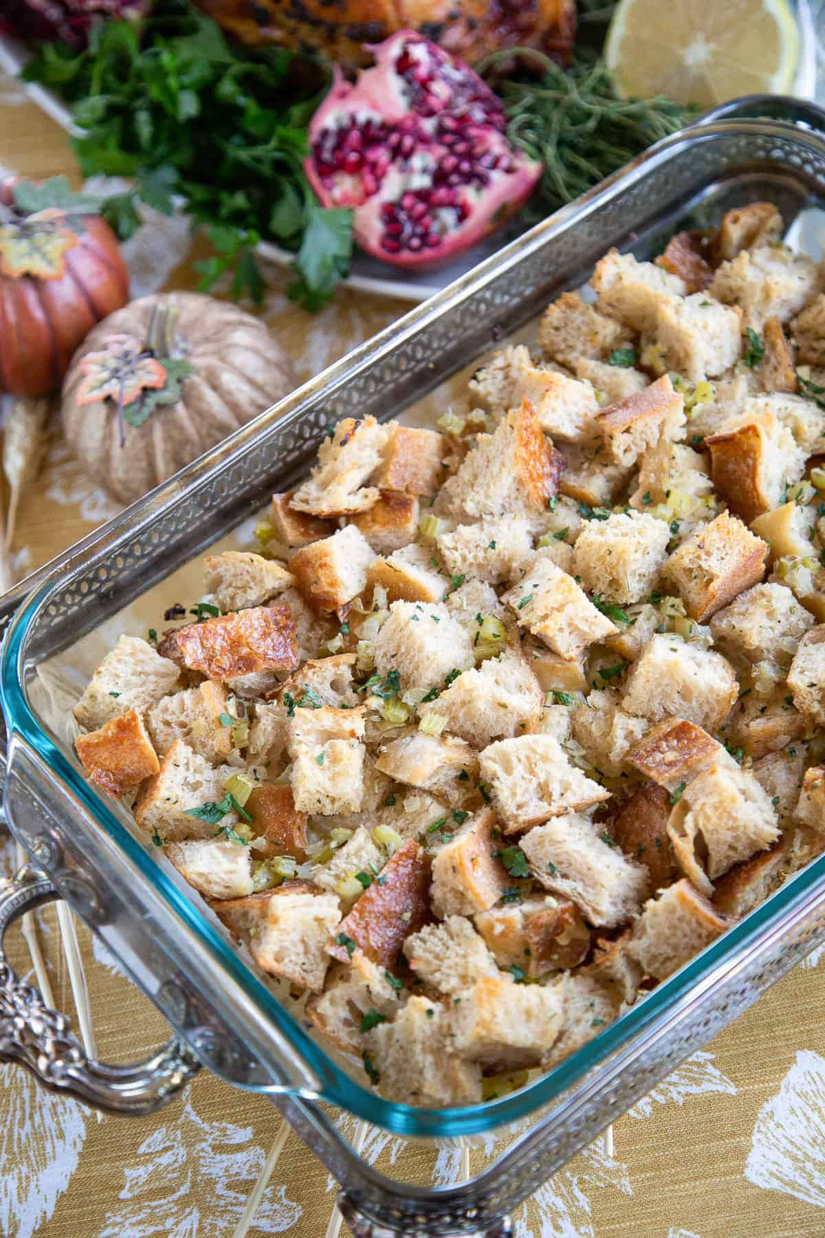 sourdough stuffing in a glass casserole dish on a table with a gold table runner and mini decorative pumpkins.