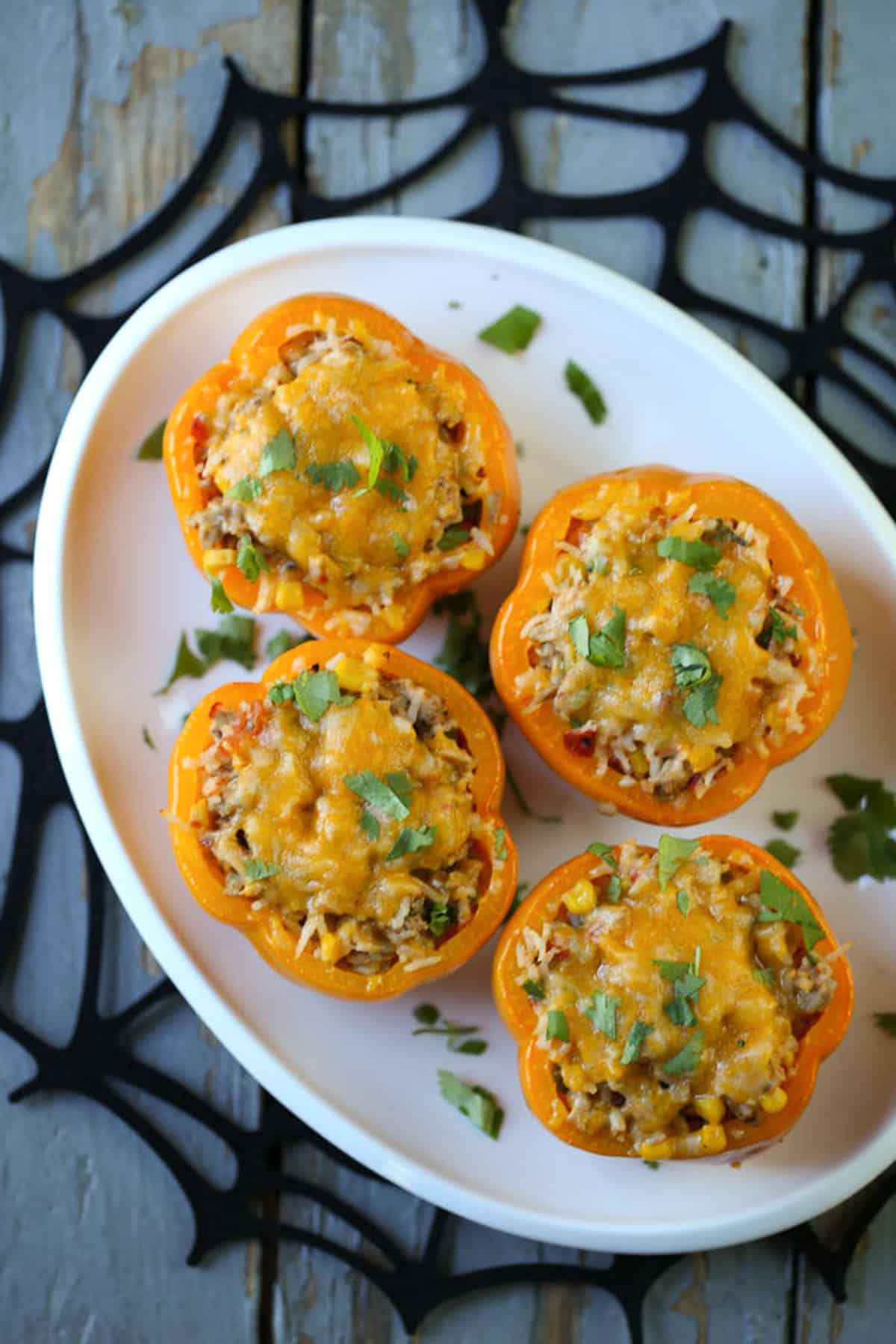 orange bell peppers stuffed with rice, ground turkey, and cheese on a white oval platter.