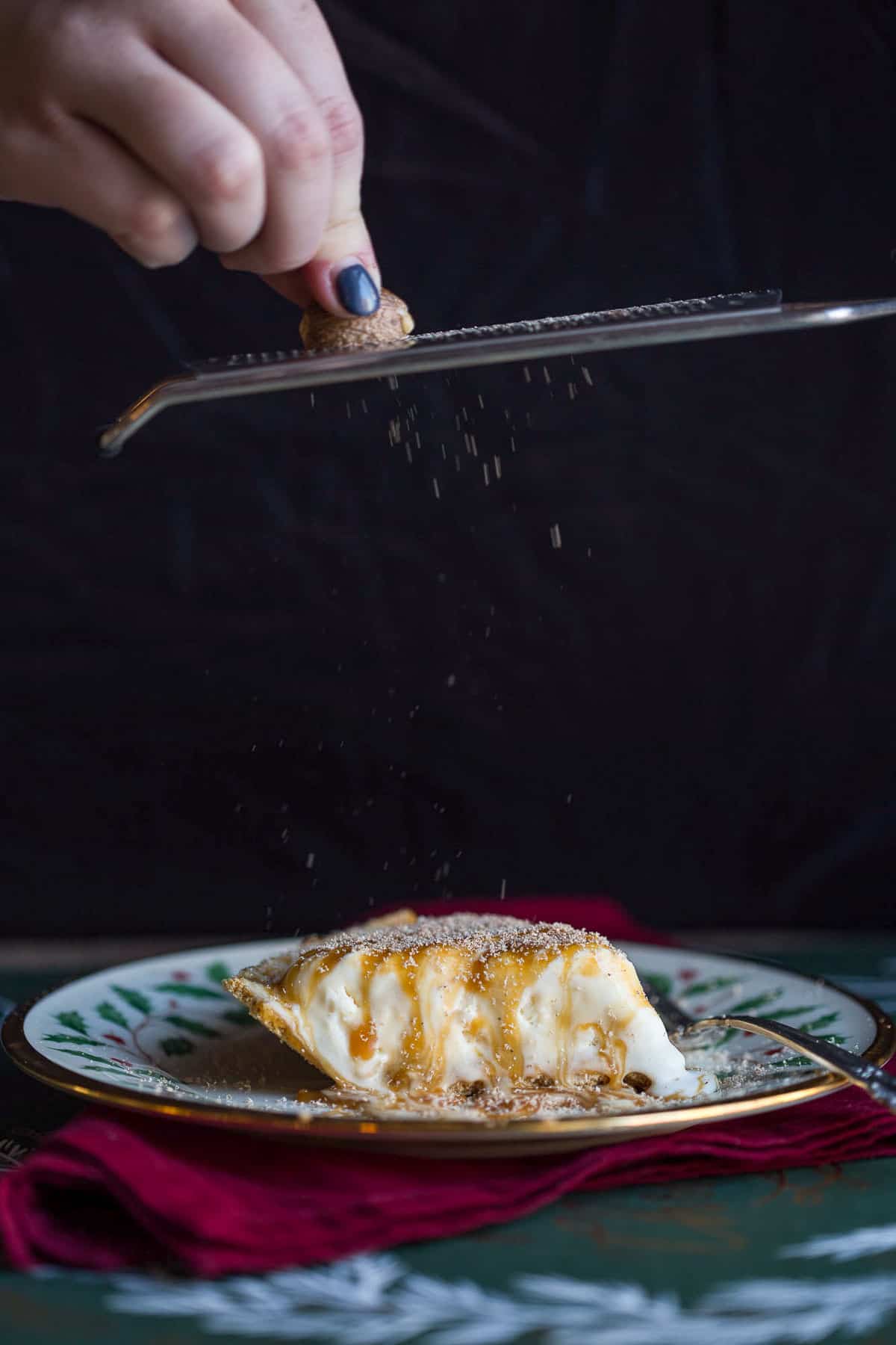 hand grating nutmeg with a microplane onto a slice of eggnog pie.