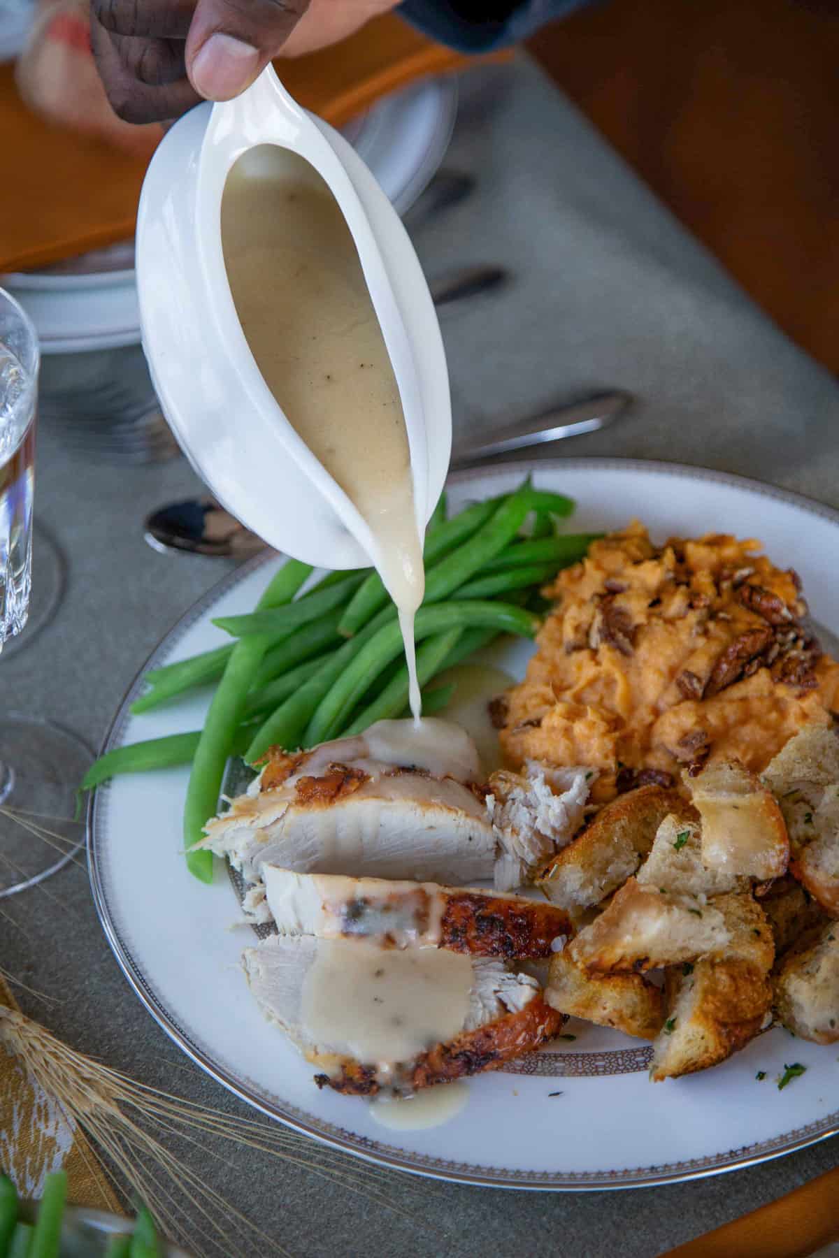 hand pouring gravy from a gravy boat onto a plate of thanksgiving food.