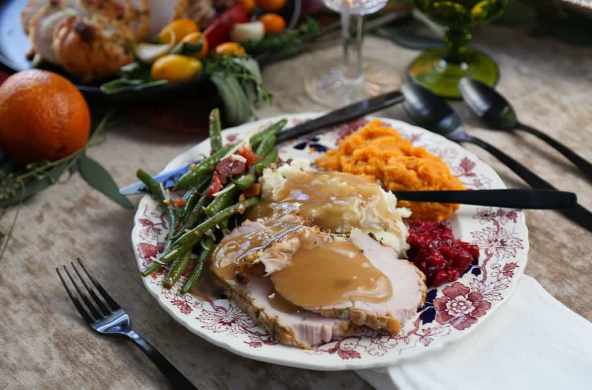 china plate filled with turkey, gravy, sweet potatoes, cranberry sauce, and green beans.