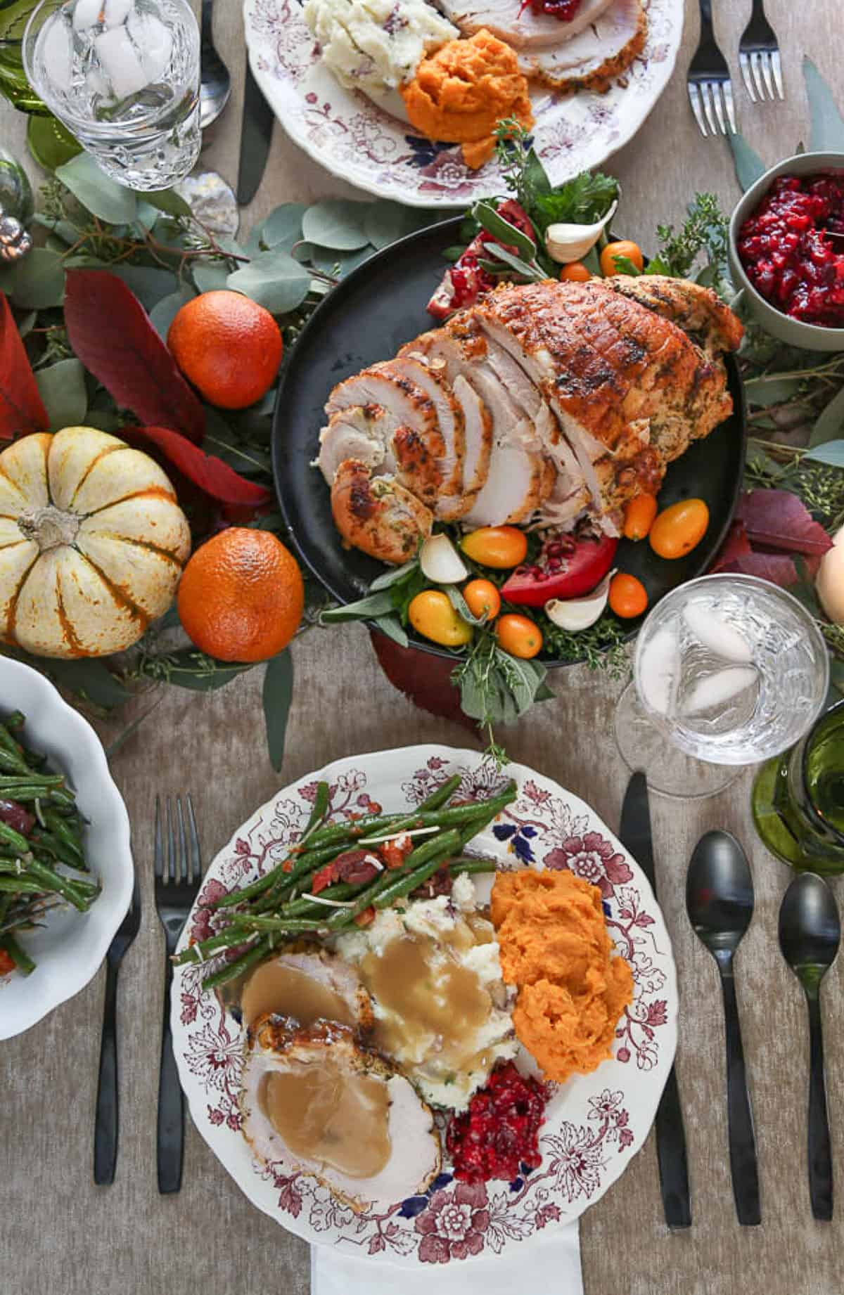 thanksgiving dinner plate on a dinner table set with turkey slices, mini pumpkins, china, and utensils.