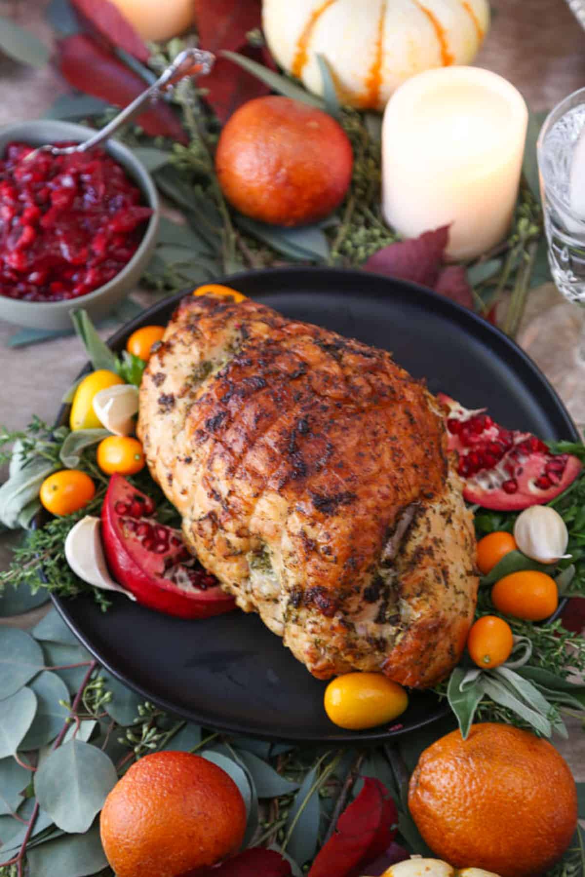 turkey breast with crispy skin on a black platter surrounded by fresh fruits and herbs.