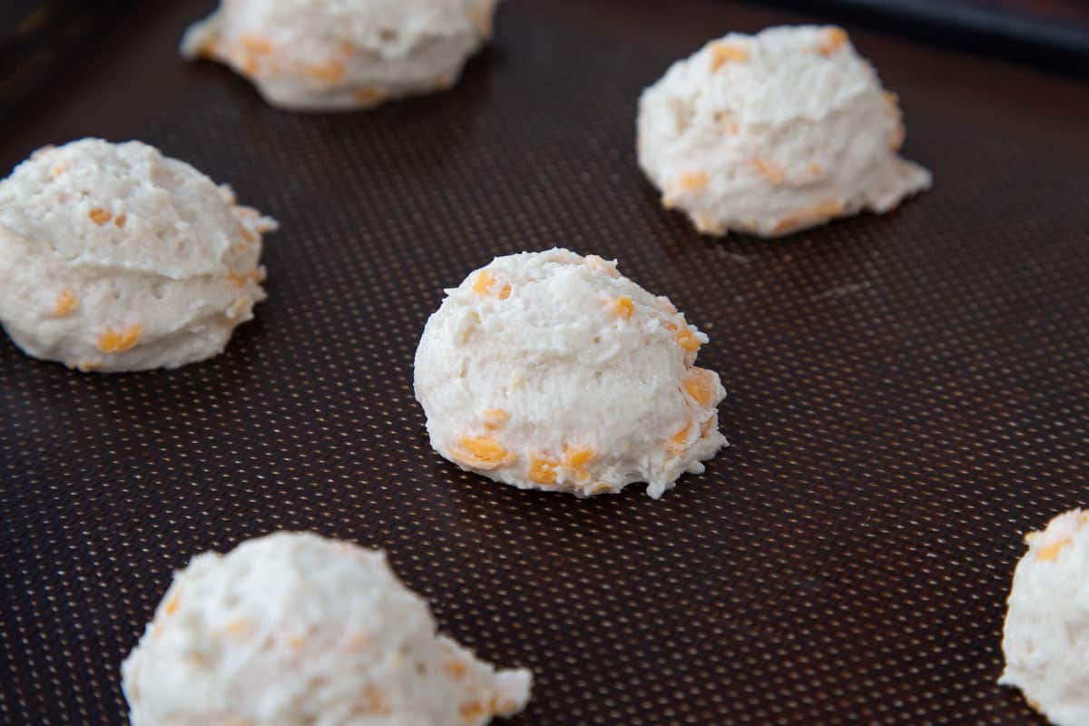 unbaked cheddar biscuits on a baking mat.