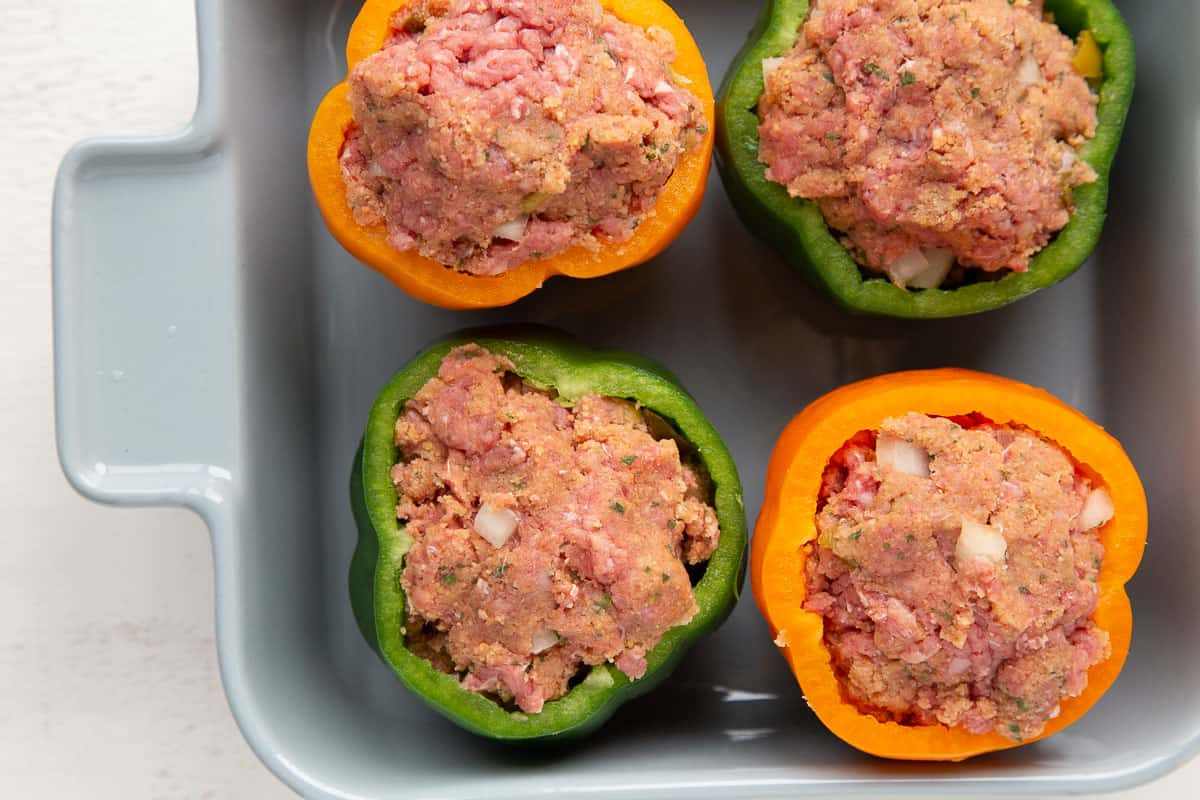 bell peppers with uncooked beef filling in a casserole dish.