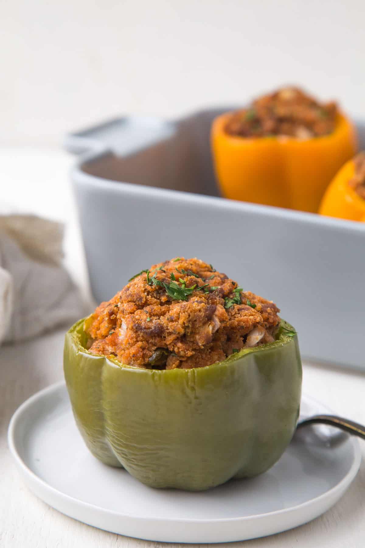 green stuffed pepper on a small white plate in front of a casserole dish with more stuffed peppers.