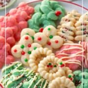 assortment of white, red, and green spritz cookies on a white cake stand with a red rim.