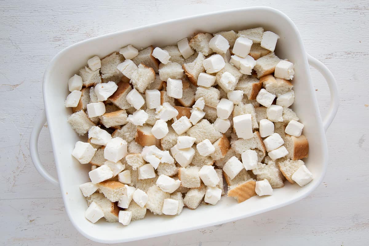 bread cubes and cubes of cream cheese in a white casserole dish.