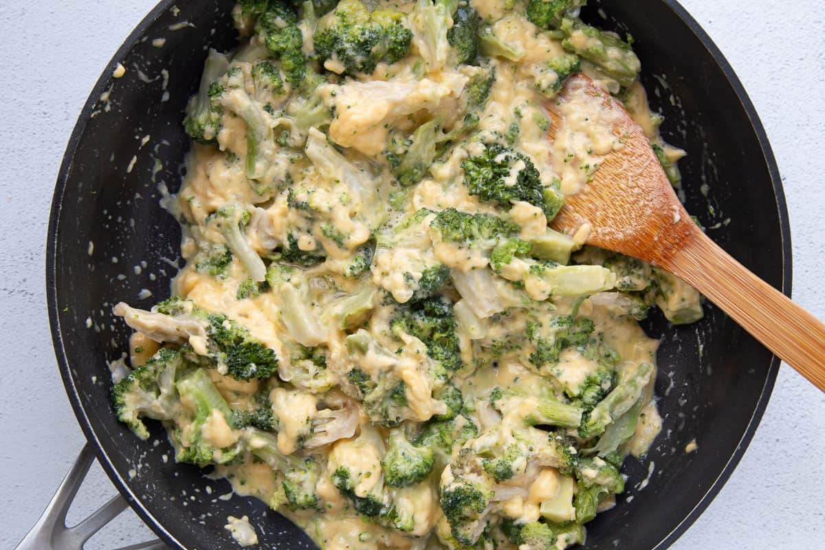 cheesy broccoli mixture in a large skillet with a wooden spoon.