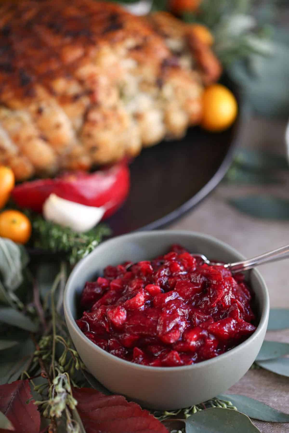 cranberry sauce in a small green bowl next to a turkey breast on a black platter.