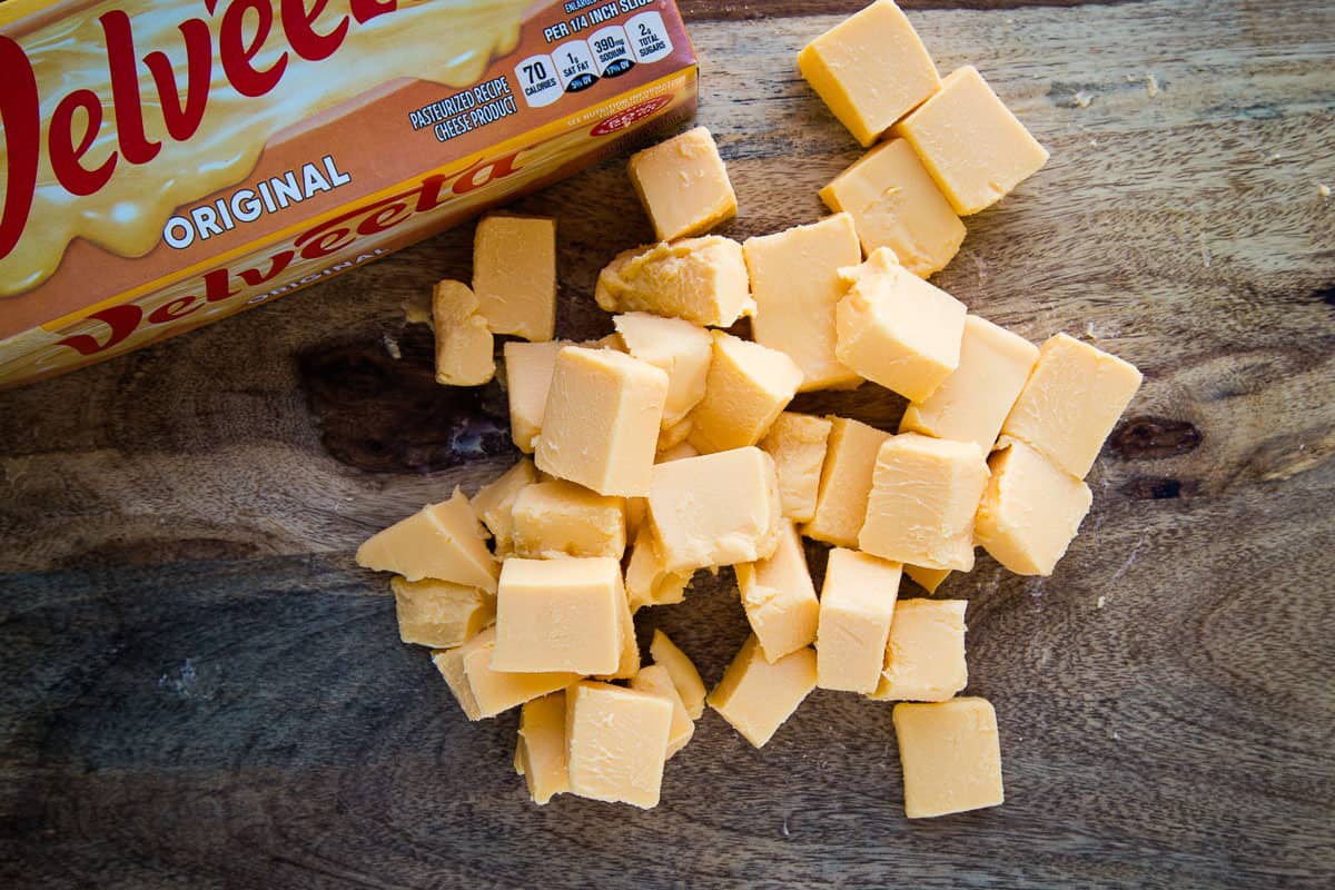 cubed Velveeta cheese on a wooden cutting board.