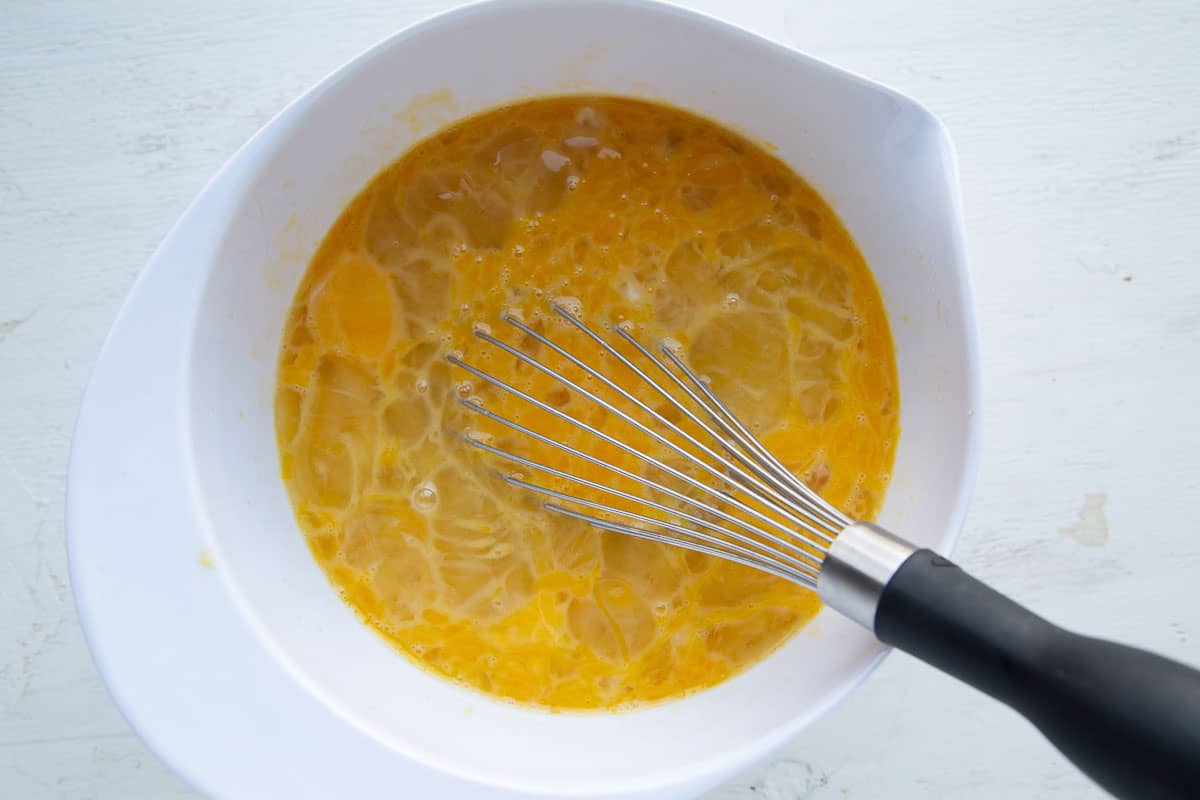 beaten eggs and a whisk in a white mixing bowl.