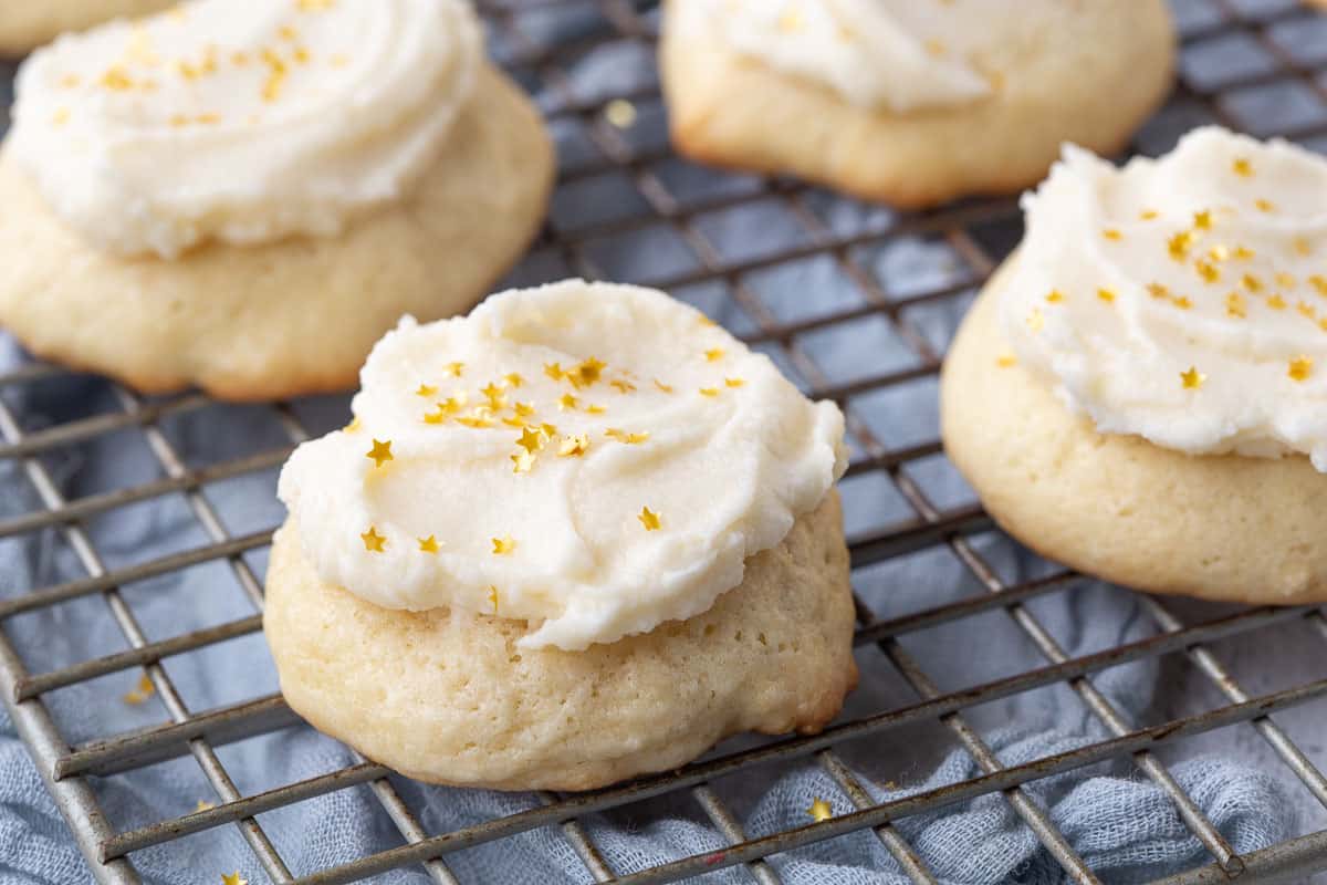 frosted sour cream cookies topped with gold star sprinkles on a wire rack.