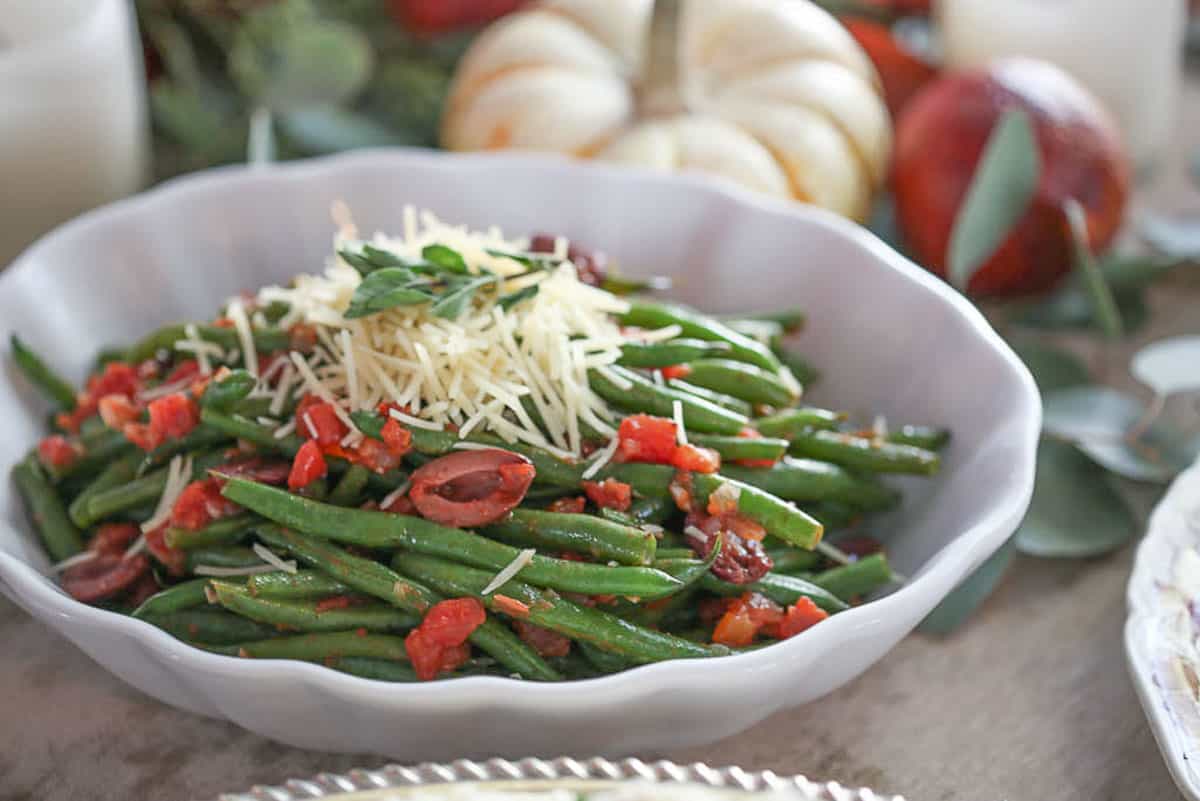 green beans in a white oval dish, topped with diced tomatoes and shredded parmesan.