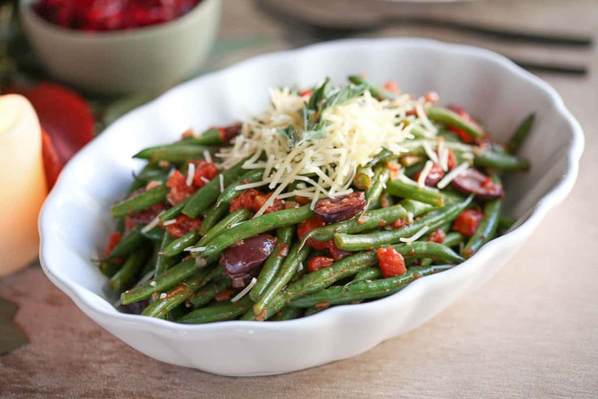 italian green beans in a white dish, topped with diced tomatoes and shredded parmesan cheese.