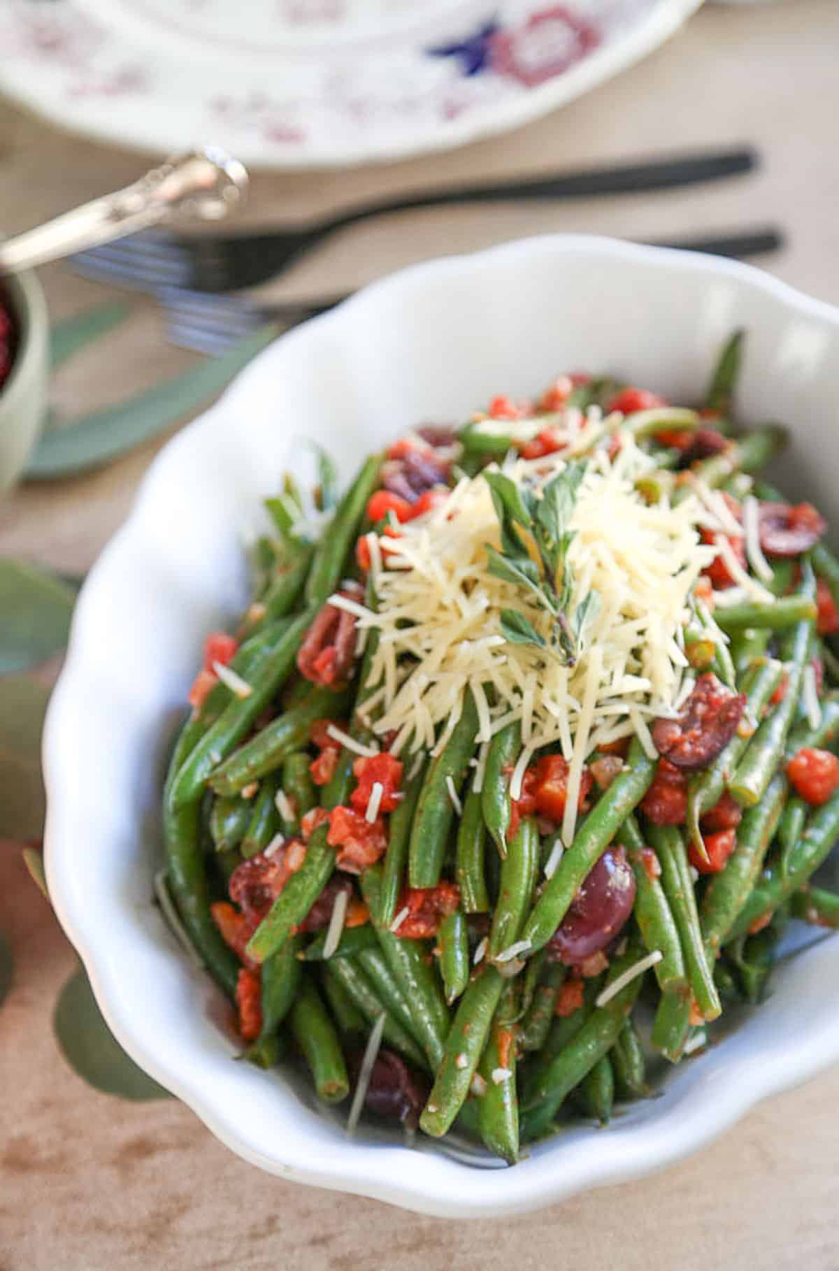green beans topped with diced tomatoes and parmesan in a white oval dish.