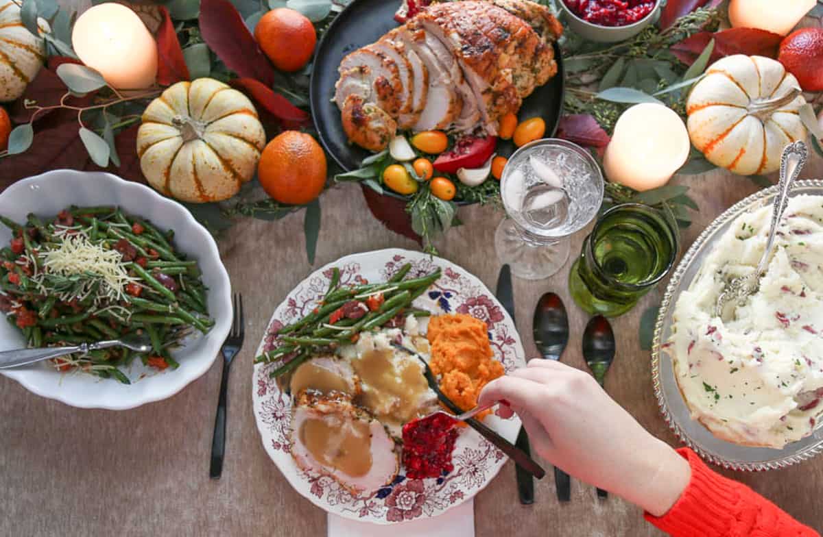 dinner table set with geren beans, mashed potatoes, turkey, mini pumpkins, and china plates filled with food.